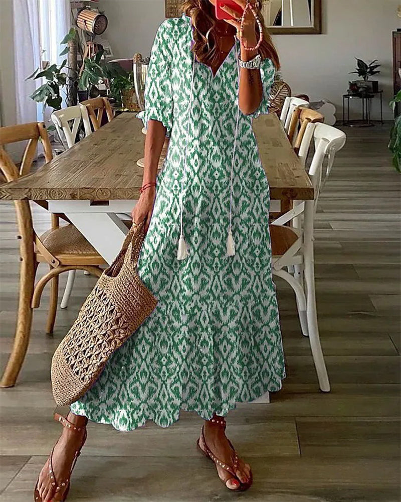 Robe longue verte à motifs géométriques portée par une femme avec un sac en osier, sandales marron, dans une salle à manger moderne.
