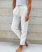 Pantalon en lin blanc pour femme, taille élastique avec cordon, poches latérales, style décontracté, fond en bois clair.