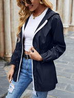 Femme portant un imperméable bleu marine, t-shirt blanc et jeans déchirés, marchant dans une rue pavée. Mode décontractée, style urbain chic.