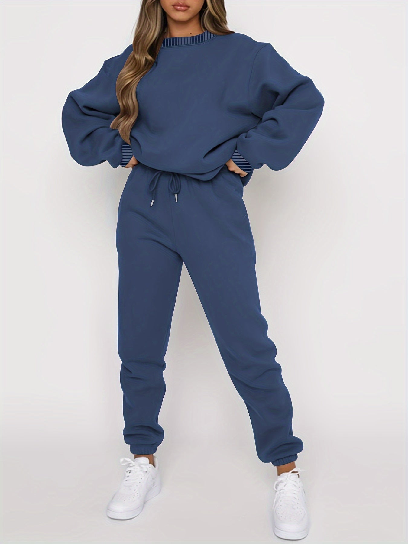 Femme portant un survêtement bleu marine, composé d'un sweat ample et d'un pantalon de jogging, avec des baskets blanches. Mode décontractée tendance.