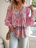 Femme portant un chemisier bohème rose à motifs floraux, manches longues, avec un sac en osier, debout près d'une fenêtre lumineuse.