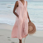Robe d'été rose sans manches sur femme à la plage, tenant un chapeau en paille. Mode estivale, tenue décontractée bord de mer.