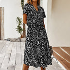 Robe noire à pois blancs, manches courtes, portée par une femme sur une terrasse en bois. Mode estivale élégante et décontractée.