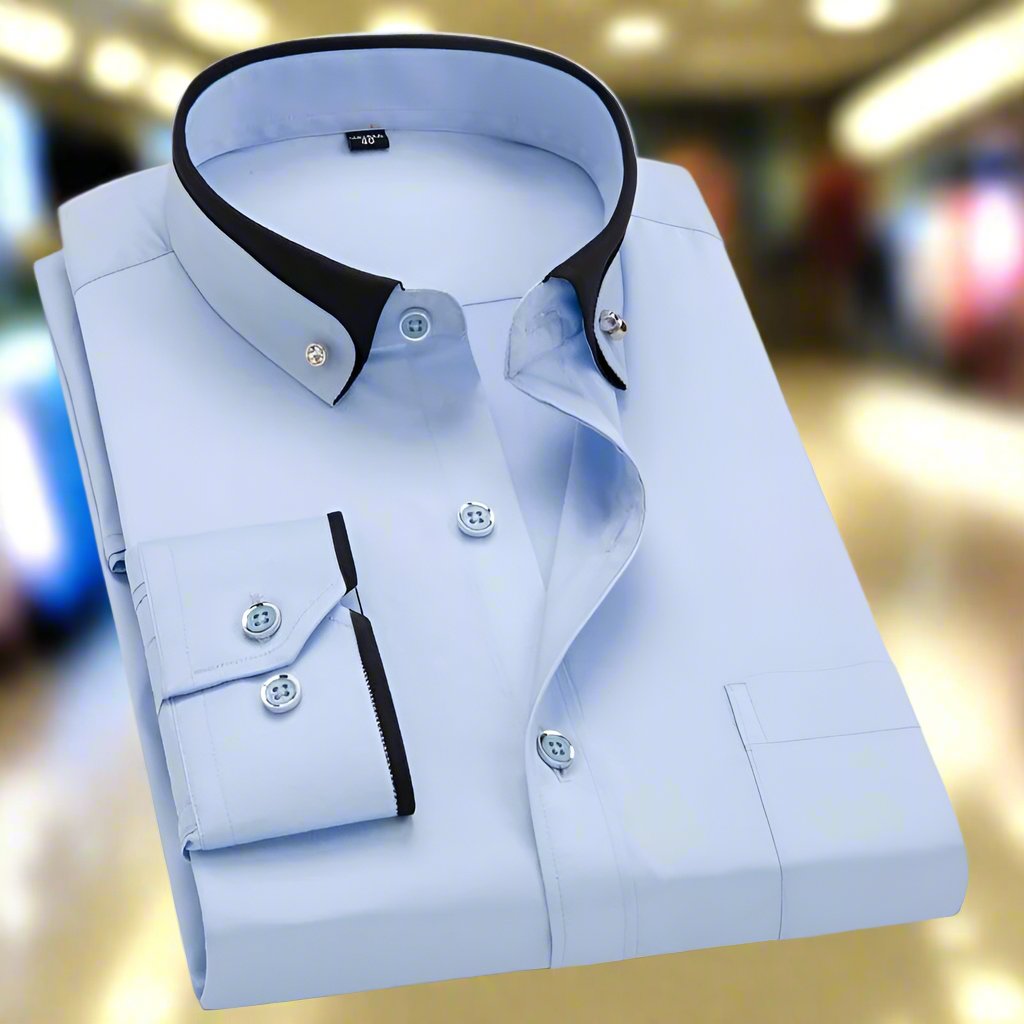 Chemise homme élégante bleu clair avec col contrasté noir, boutons assortis, manches longues, posée sur fond flou de magasin. Mode masculine chic.