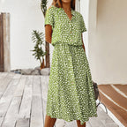 Robe verte à pois blancs, manches courtes, col en V, portée par une femme sur une terrasse en bois. Mode estivale, tenue décontractée élégante.