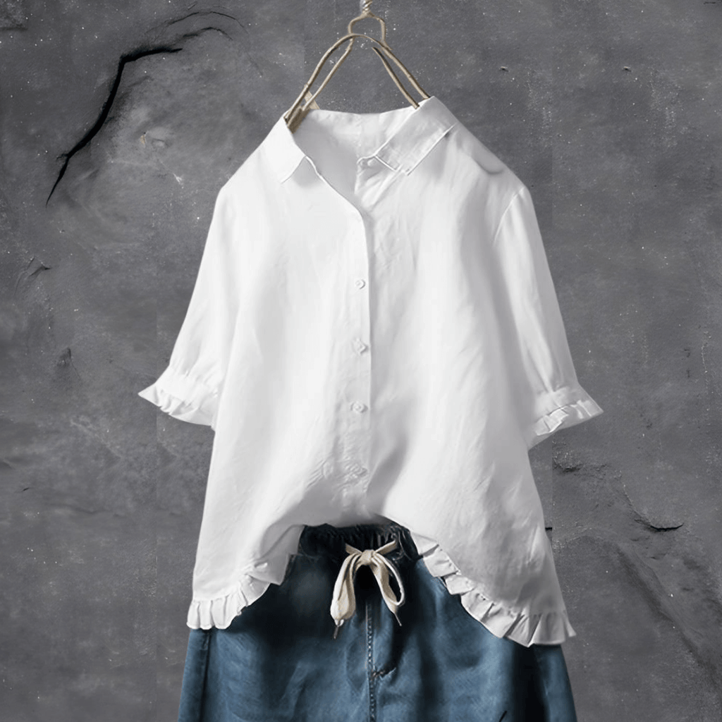 Chemisier blanc élégant avec manches courtes et volants, suspendu sur un cintre, sur fond gris texturé. Mode féminine, style décontracté.