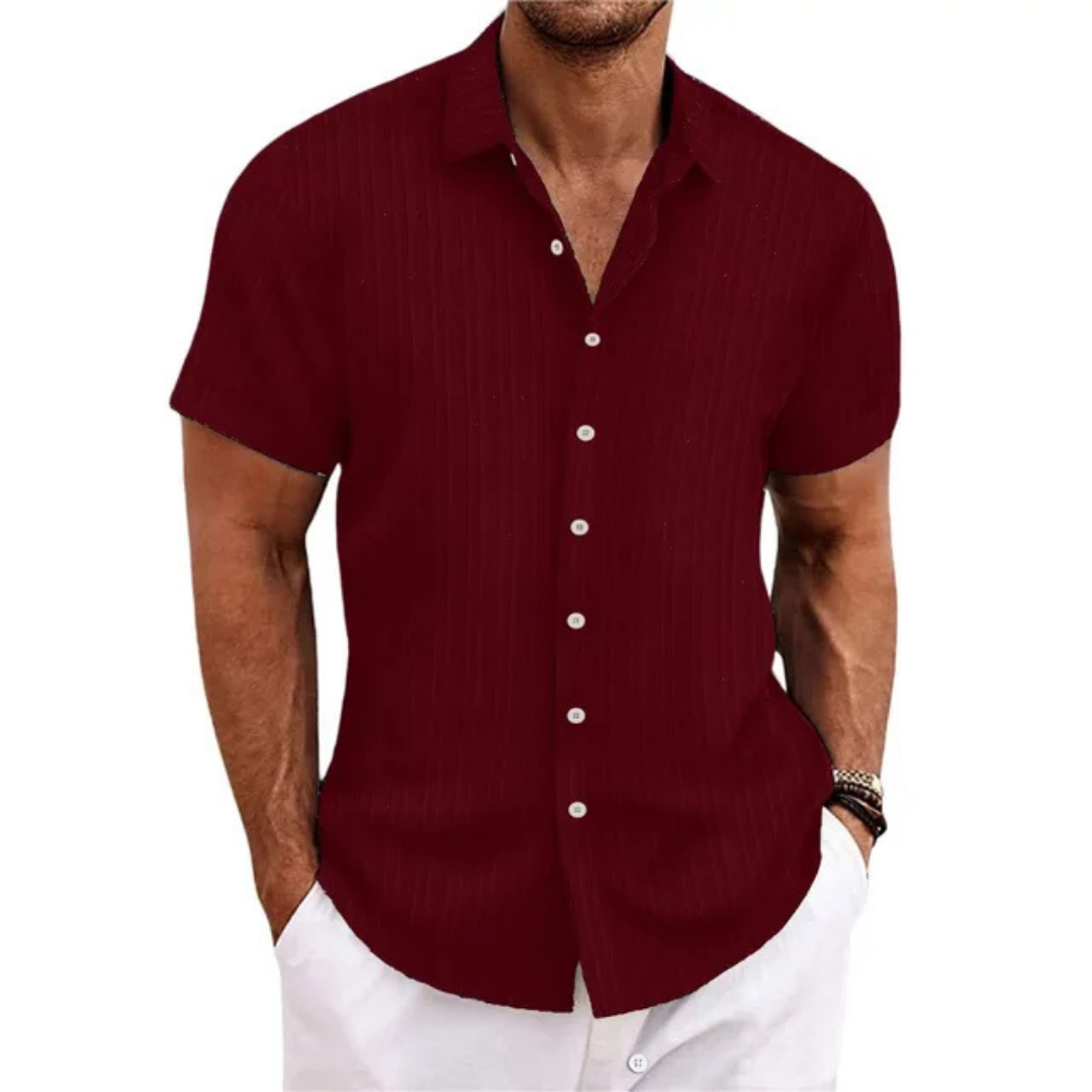 Chemise homme bordeaux à manches courtes, col ouvert, boutons blancs, portée avec un pantalon blanc. Mode masculine élégante et décontractée.