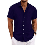 Homme portant une chemise bleu marine à manches courtes avec boutons blancs, style décontracté, associée à un pantalon blanc. Mode masculine élégante.