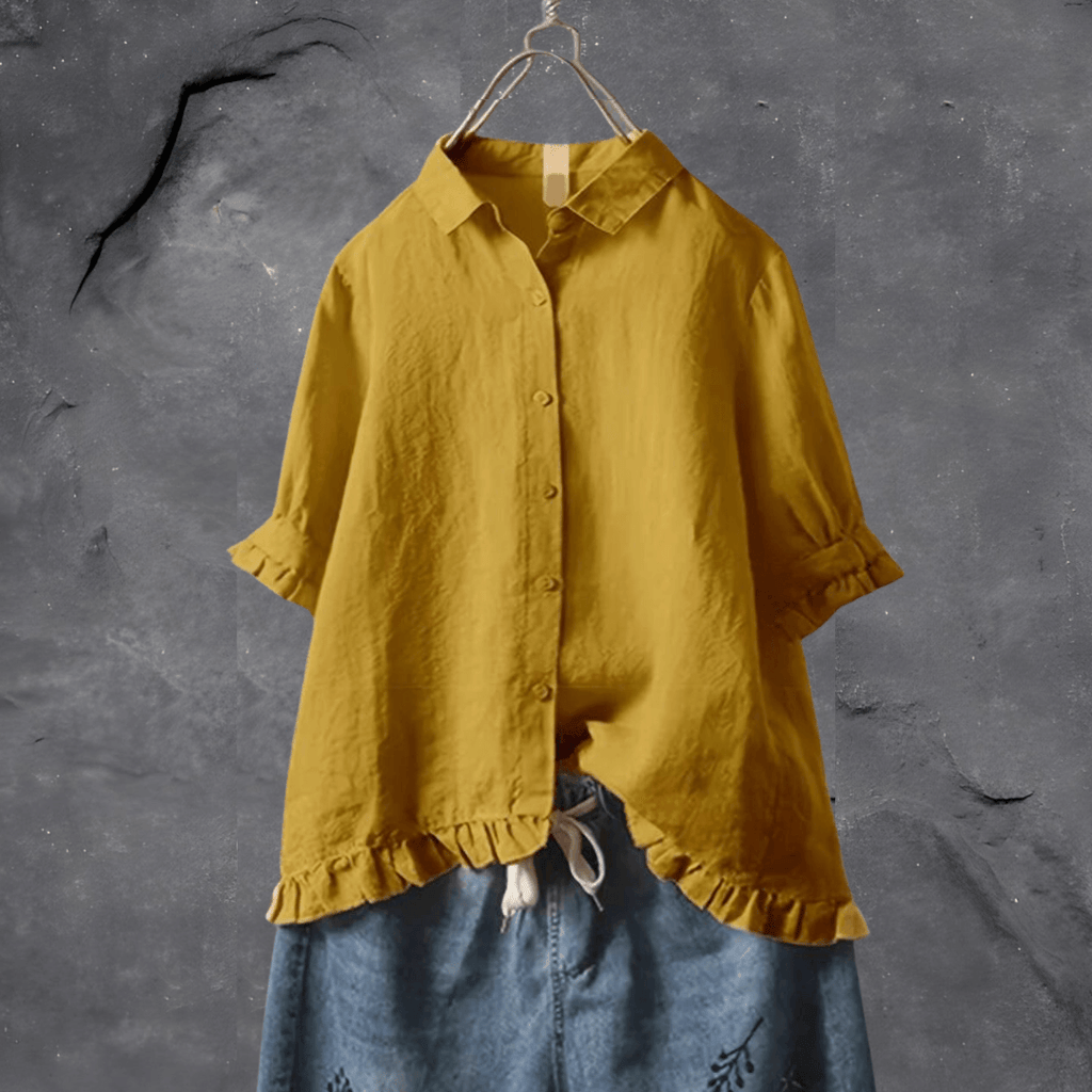 Chemise jaune moutarde en lin sur cintre, manches retroussées, devant mur gris texturé. Mode éco-responsable, style décontracté, tendance automne.