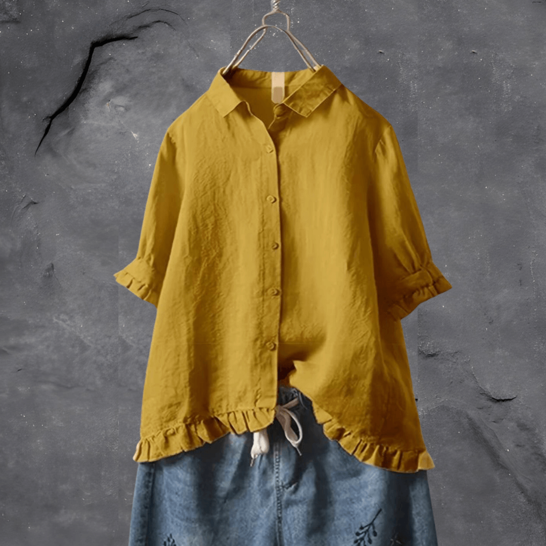 Chemise jaune moutarde en lin sur cintre, manches retroussées, devant mur gris texturé. Mode éco-responsable, style décontracté, tendance automne.