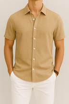 Chemise beige à manches courtes pour homme, boutons blancs, col classique, portée avec un pantalon blanc. Mode masculine élégante et décontractée.