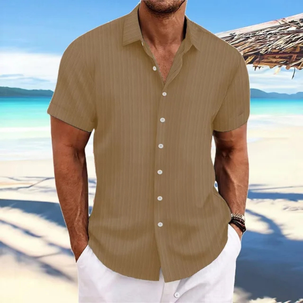 Homme en chemise marron à manches courtes sur plage tropicale, mer turquoise en arrière-plan, ciel bleu, style estival décontracté.
