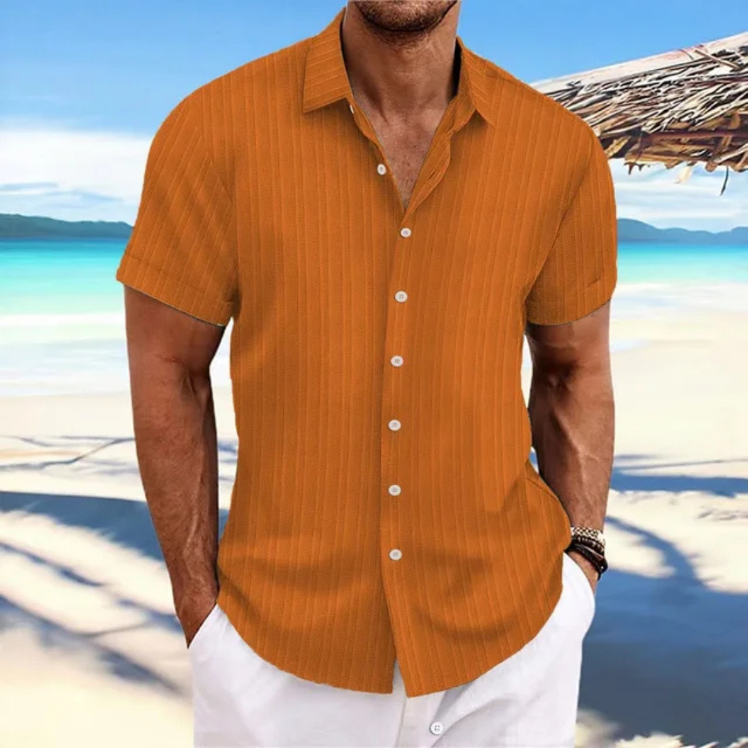 Homme en chemise orange à manches courtes sur plage tropicale, mer turquoise en arrière-plan, ciel bleu, vacances d'été, mode décontractée.