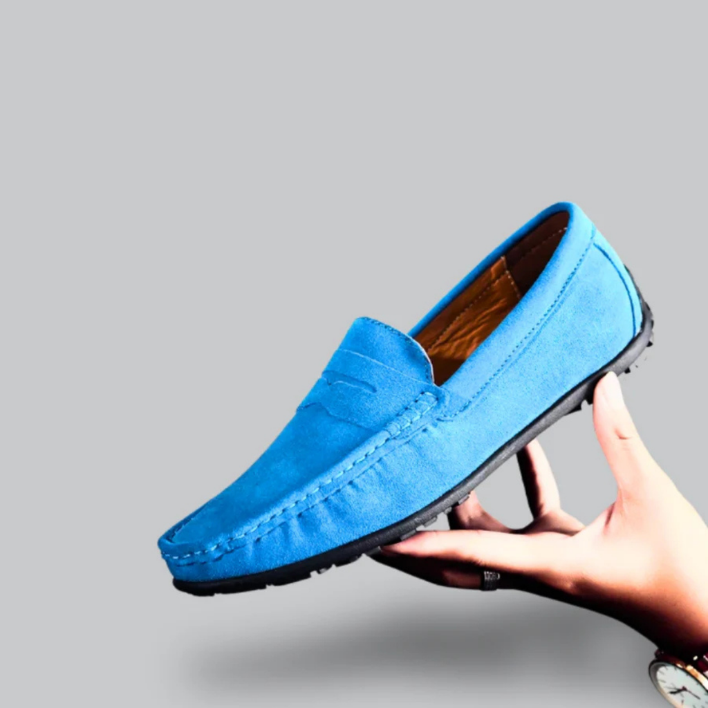 Mocassin bleu en daim pour homme, semelle noire, tenu par une main. Chaussure élégante et confortable, idéale pour un style décontracté.