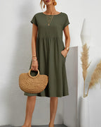 Robe verte décontractée avec manches courtes, portée par une femme tenant un sac en paille. Décor minimaliste avec vase et pampas. Mode été chic.