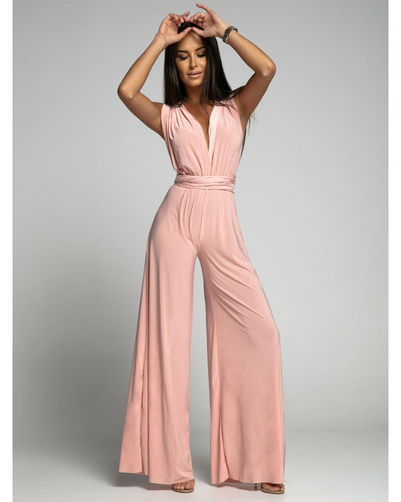 Femme portant une combinaison rose élégante, sans manches, avec jambes larges, posant sur fond neutre. Mode féminine, tenue chic, style moderne.