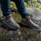 Chaussures de randonnée imperméables sur un randonneur traversant un ruisseau en forêt, idéales pour activités extérieures et terrains humides.