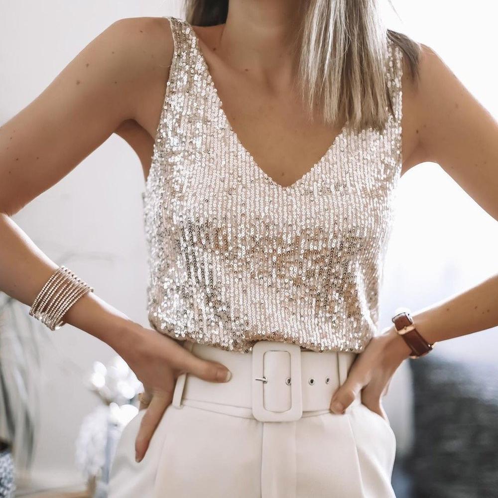 Femme portant un débardeur à paillettes argentées, ceinture blanche et bracelet élégant. Mode chic, tenue de soirée glamour.