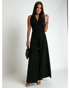 Femme portant une élégante combinaison noire sans manches, tenant un sac à main noir. Mode chic, tenue de soirée, style moderne.