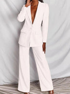 Femme en tailleur pantalon blanc élégant, veste à col profond, posant devant un fond neutre. Mode chic, tenue professionnelle féminine.