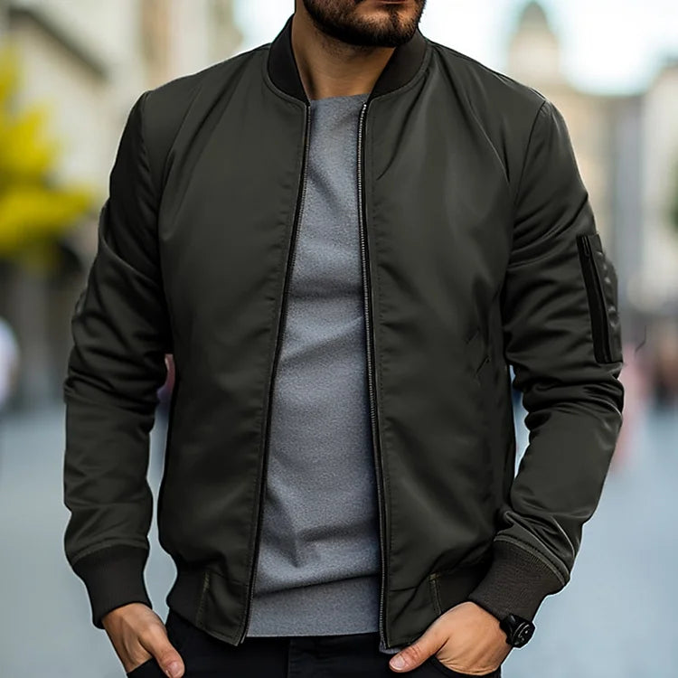 Homme portant un blouson bomber vert foncé, t-shirt gris, montre noire, en ville. Mode masculine, style urbain, tendance automne.