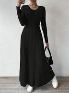 Robe longue noire côtelée, manches longues, portée avec des baskets blanches et un sac à main noir. Mode élégante et décontractée pour femme.