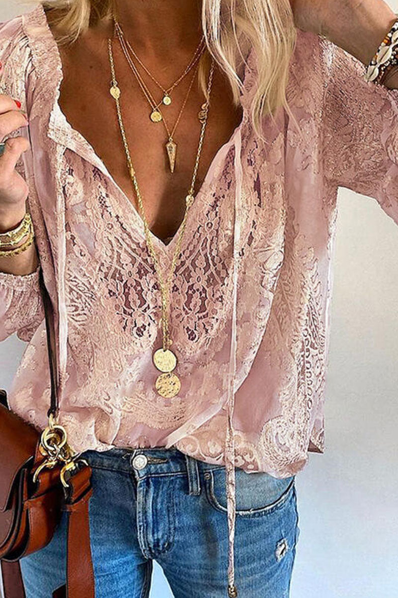 Blouse en dentelle rose élégante avec col en V, portée avec des colliers dorés superposés et un jean décontracté. Mode féminine chic et tendance.
