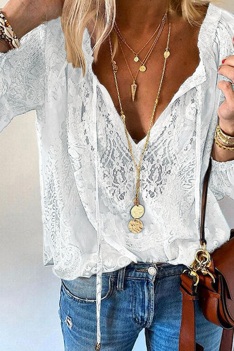 Femme portant un chemisier en dentelle blanche avec col en V, colliers dorés superposés, jean bleu décontracté et sac marron. Mode élégante et tendance.