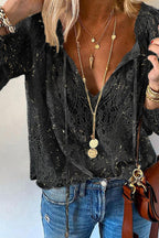 Femme portant un chemisier en dentelle noire avec col en V, colliers dorés superposés, jean bleu et sac marron. Mode élégante et tendance.