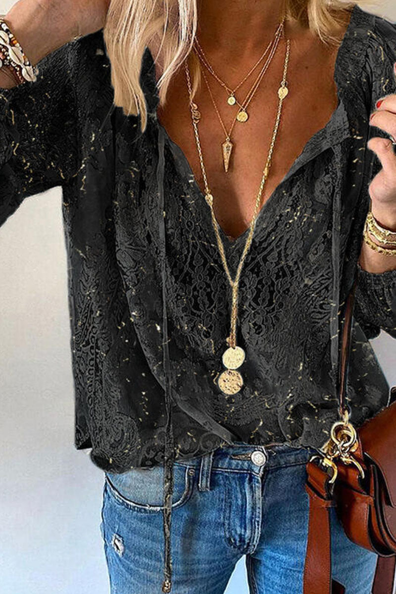 Femme portant un chemisier en dentelle noire avec col en V, colliers dorés superposés, jean bleu et sac marron. Mode élégante et tendance.
