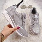 Chaussures de sport argentées brillantes avec fermeture éclair, posées sur un tapis blanc, accompagnées de lunettes de soleil et d'une montre-bracelet.