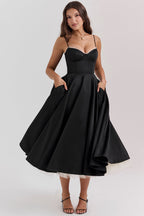 Robe noire élégante avec jupe évasée, bretelles fines et poches, portée par une femme. Mode féminine chic, tenue de soirée glamour.
