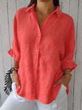 Chemise en lin corail pour femme, manches retroussées, col classique, portée avec un pantalon blanc. Mode estivale élégante et décontractée.