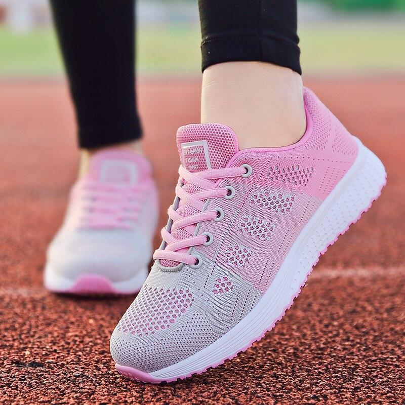 Baskets de course roses et grises sur piste d'athlétisme, chaussures de sport légères pour femme, design respirant, semelle blanche antidérapante.