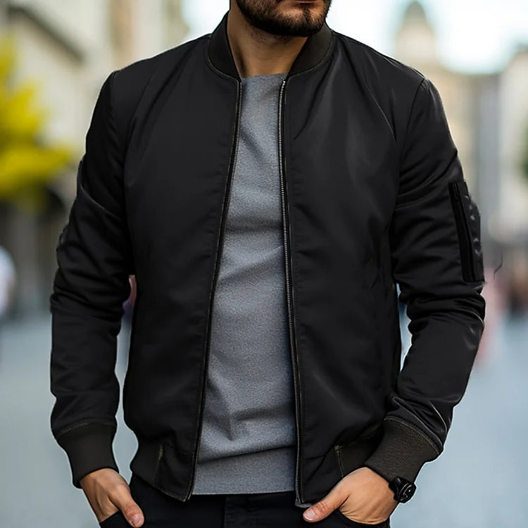 Homme portant un blouson bomber noir, t-shirt gris, montre noire, en ville. Mode masculine, style urbain, tenue décontractée.
