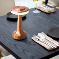 Lampe de table en cuivre moderne sur une table en bois sombre, entourée de couverts élégants et de verres à vin, créant une ambiance chic et sophistiquée.
