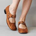 Chaussures Mary Jane marron en cuir avec boucle, talon bas, portées par une personne debout. Mode féminine, chaussures confortables, style rétro.