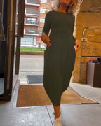 Femme en robe longue verte sortant d'un bâtiment, cheveux bouclés, baskets blanches, fond urbain. Mode décontractée, style moderne.