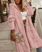 Femme portant un long cardigan rose en tricot, sac à main beige à chaîne, top blanc, pantalon imprimé, mode urbaine chic, rue pavée.