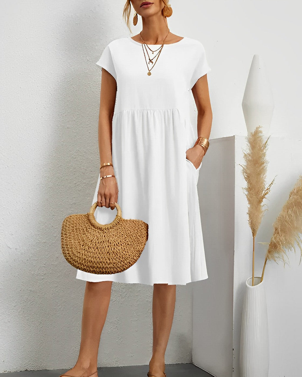Robe blanche élégante avec manches courtes, accessoires dorés, sac en osier, décor minimaliste, vase moderne, pampas. Mode féminine chic et estivale.