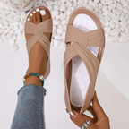 Sandales beiges croisées pour femme, posées sur un fond de galets blancs. Mode estivale, chaussures confortables, tendance 2023.