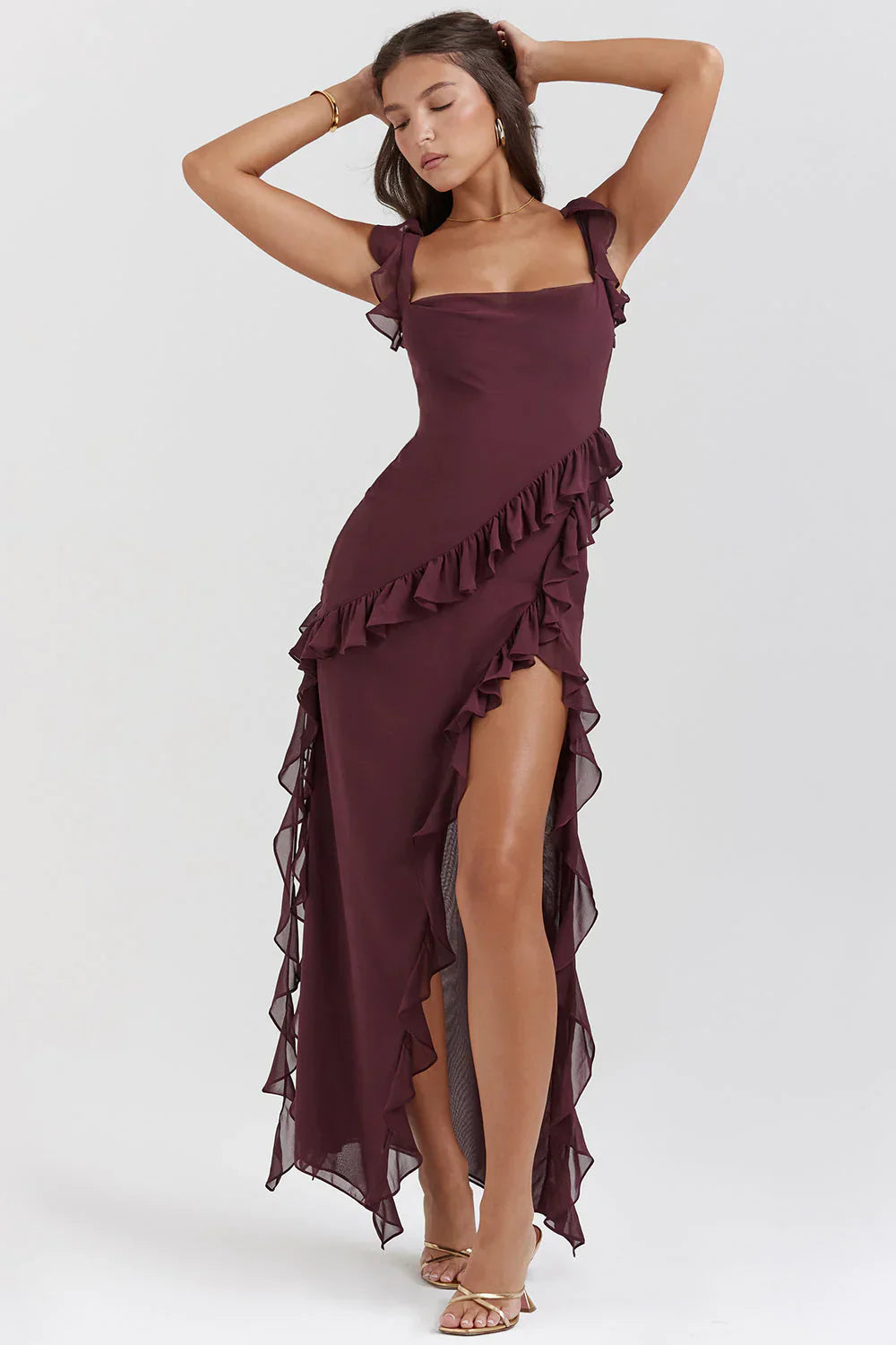 Femme portant une robe longue bordeaux à volants, élégante et chic, posant sur fond neutre. Mode féminine, tenue de soirée glamour.