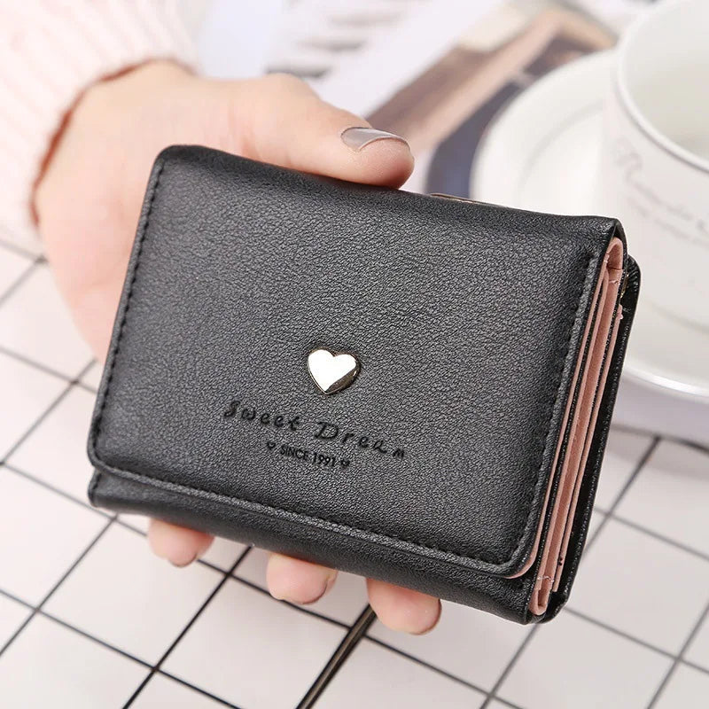 Portefeuille en cuir noir avec un motif de cœur doré, tenu par une main. Accessoire élégant pour femmes, idéal pour organiser cartes et billets.