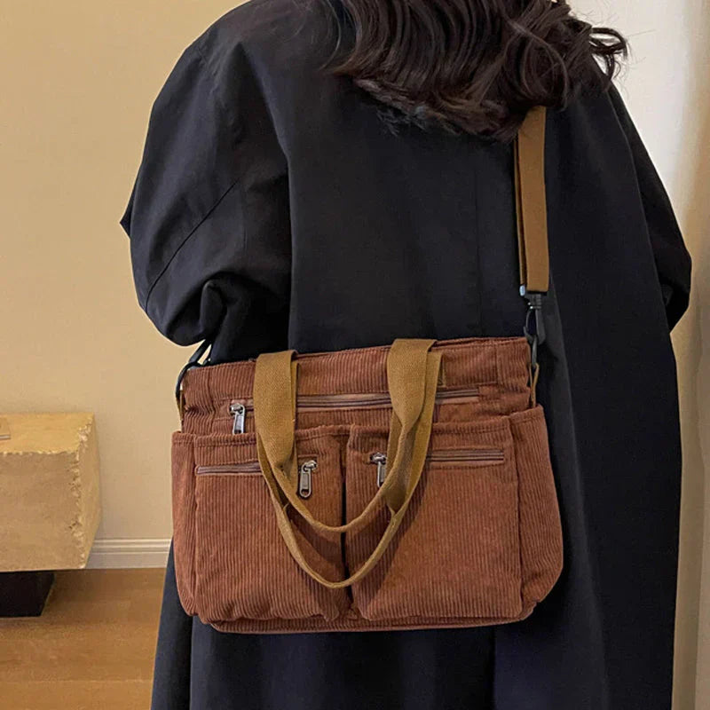 Sac à main en velours côtelé marron avec bandoulière, porté par une personne en manteau noir. Accessoire mode tendance, pratique et élégant.