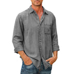 Homme portant une chemise en jean gris délavé avec manches longues retroussées, poche poitrine, et jeans bleus. Mode décontractée masculine.