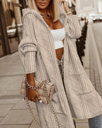 Femme portant un long cardigan beige à motifs, avec un sac à main matelassé beige à chaîne dorée, marchant en ville. Mode automne chic.