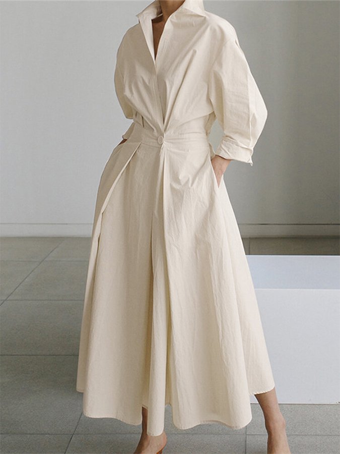 Robe longue beige élégante avec manches trois-quarts, col ouvert et ceinture à la taille, posée sur fond minimaliste. Mode féminine chic.