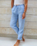 Pantalon en lin bleu clair pour femme, taille élastique avec cordon, poches latérales, style décontracté, fond en bois clair.