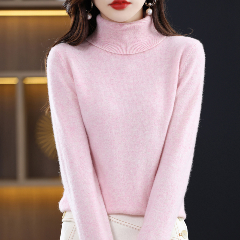 Femme portant un pull rose à col roulé, élégante et moderne, fond intérieur flou. Mode féminine automne-hiver, style chic et tendance.