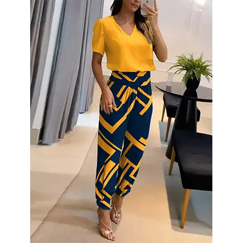 Femme en tenue élégante, chemisier jaune vif et pantalon bleu à motifs géométriques, posant dans un salon moderne. Mode féminine chic et tendance.